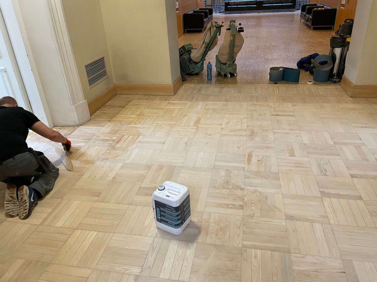 Zdjęcie przedstawia fragment podłogi drewnianej w budynku Uniwersytetu Warszawskiego, który został wycyklinowany.