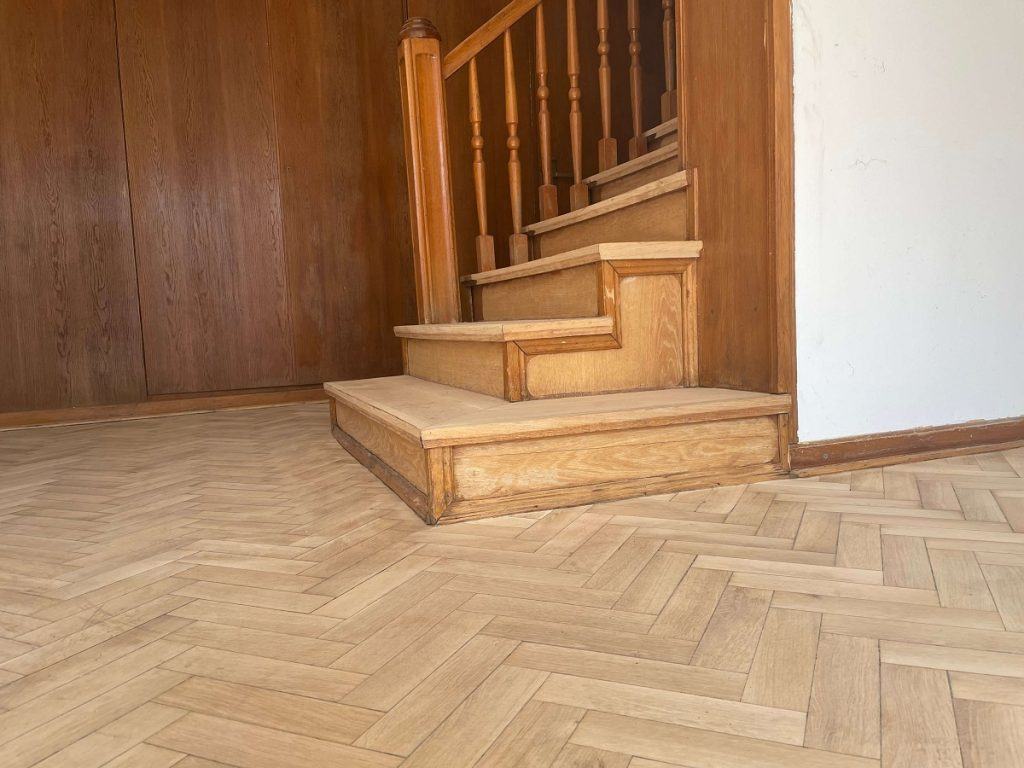 Zdjęcie prezentuje efekty cyklinowania parkietu dębowego. Widoczne są również schody, które zostaną poddane renowacji.