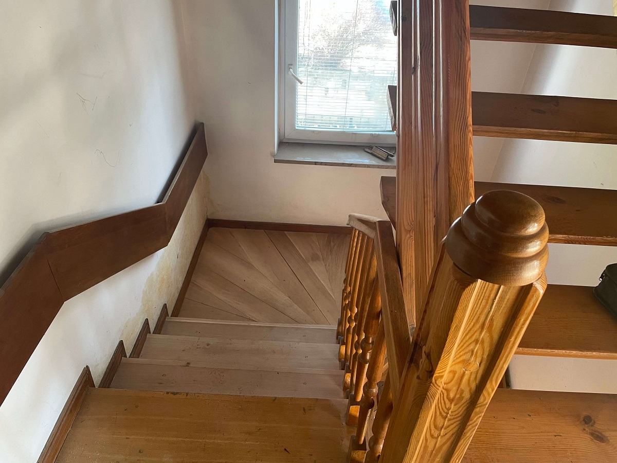 Widok z góry na drewniane schody w domu jednorodzinnym, które poddawane są procesom cyklinowania, naprawiania i renowacji.