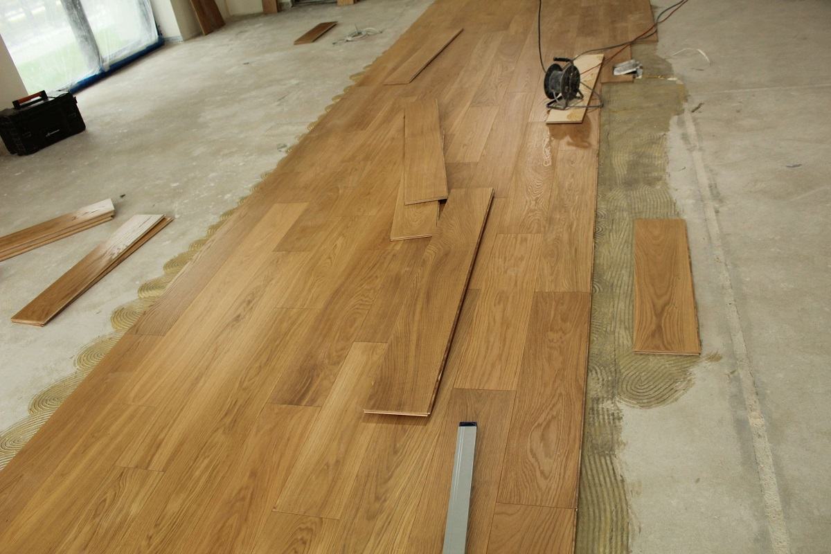Zdjęcie prezentuje postępy prac podczas układania drewnianej, dębowej podłogi we wzór pokładowy.