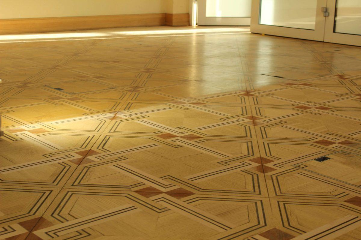 Zdjęcie pokazuje drewnianą podłogę pałacową w budynku Uniwersytetu Warszawskiego przed zabiegiem renowacji.