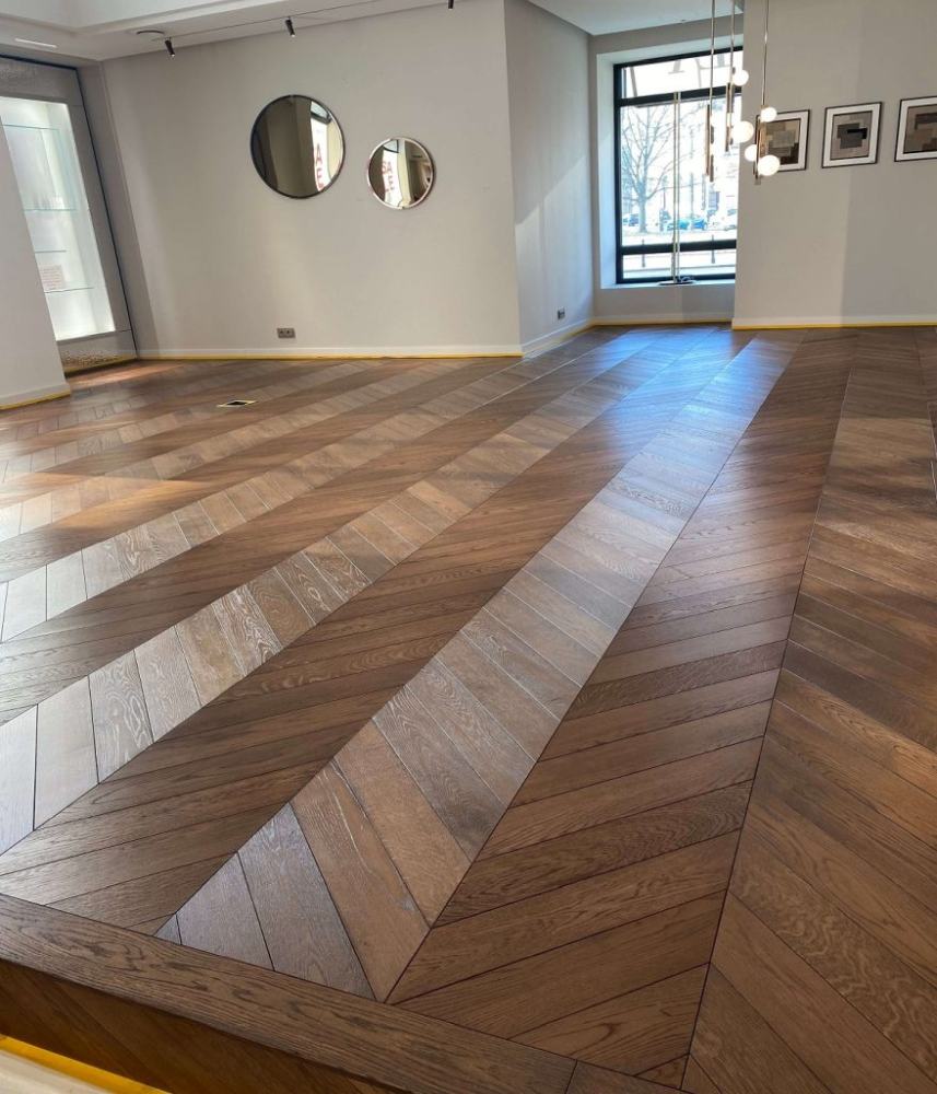 Na zdjęciu widzimy podłogę dębową o wzorze klepek ułożonych w jodełkę, która została poddana zabiegom cyklinowania oraz koloryzowania.