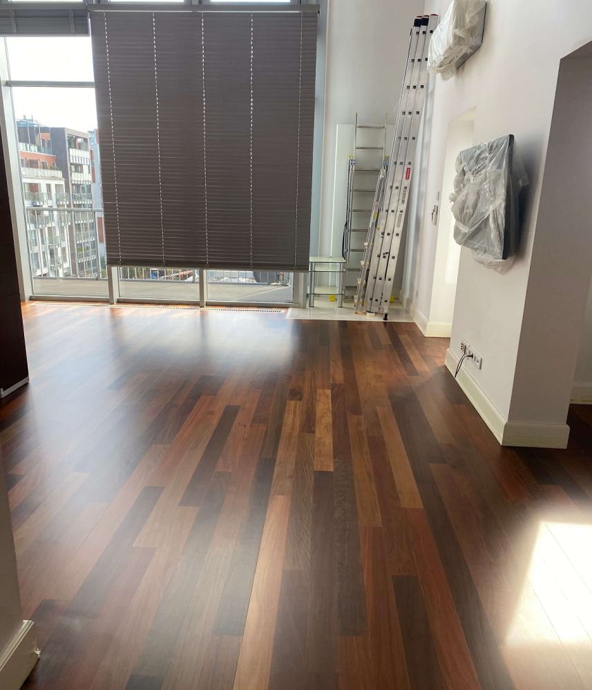 Zdjęcie przedstawia pomieszczenie w którym wycyklinowano oraz polakierowano podłogę wykonaną z egzotycznego drewna merbau.