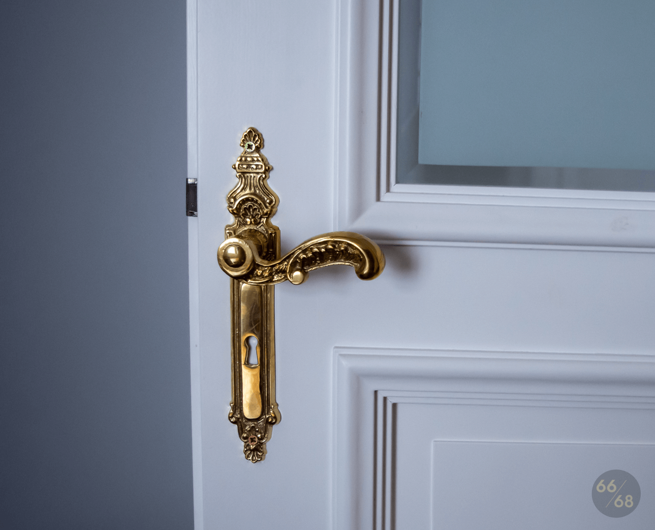 Na zdjęciu widoczny fragment drzwi ze zdobną złotą klamką stylizowaną na antyk.