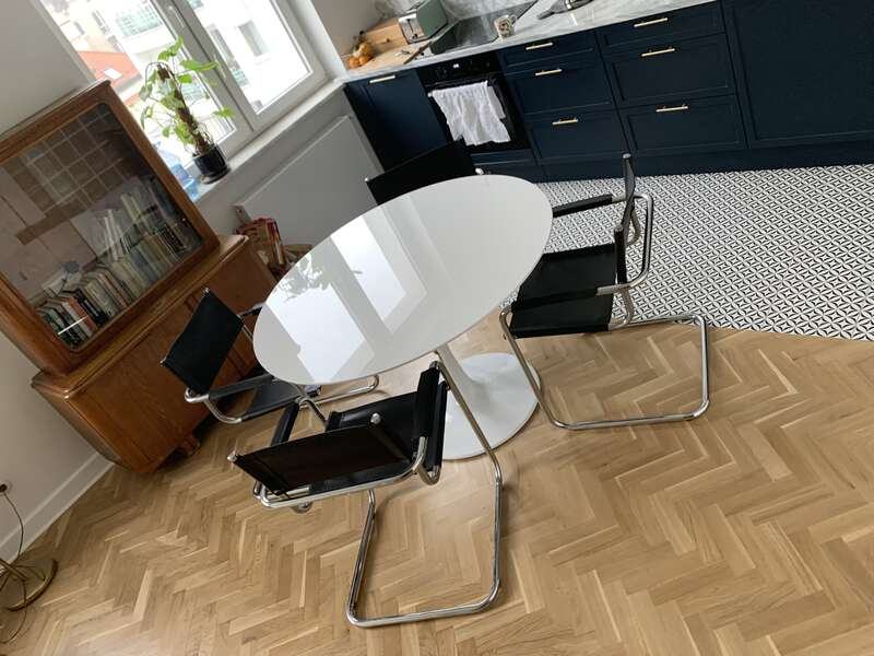 Zdjęcie przedstawia fragment jadalni z okrągłym stołem i 4 krzesłami. Widoczna jest również podłoga z parkietem ułożonym z drewnianych klepek we wzór jodełki.