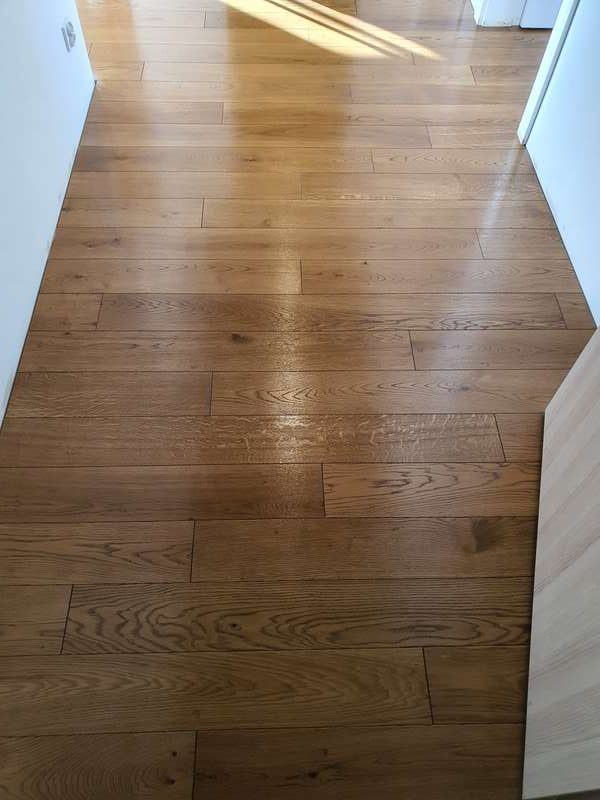 Zdjęcie pokazuje drewnianą podłogę, ułożoną we wzór pokładowy z dębowych desek, która błyszczy po dokonanej konserwacji twardym woskiem.