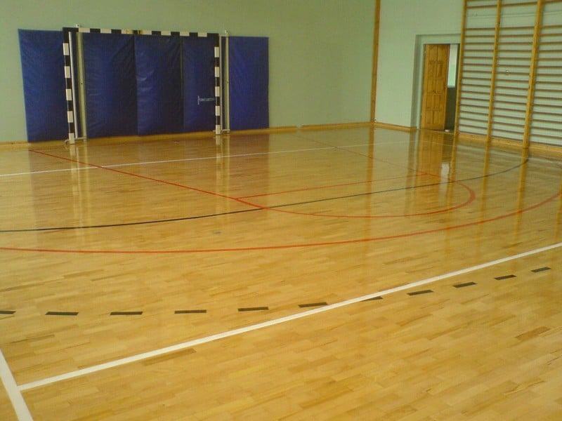 Zdjęcie przedstawia salę sportową z gotowym parkietem drewnianym, z wymalowanymi liniami boisk, która zabezpieczona została specjalistycznym lakierem.