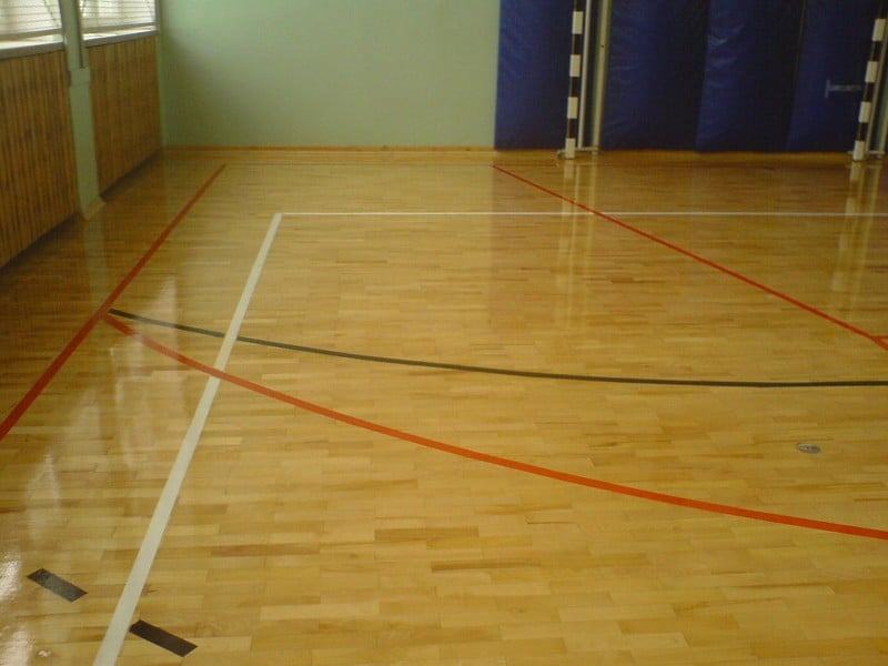 Na zdjęciu widzimy wnętrze sali sportowej. Podłoga pokryta jest drewnianym parkietem, na którym zostały wymalowane linie boisk. Całość zabezpieczono lakierem.