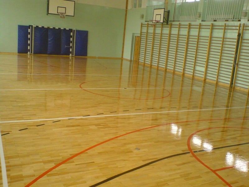 Zdjęcie prezentuje salę gimnastyczną ze specjalistycznym parkietem drewnianym z liniami boiskowymi, która zabezpieczona jest odpowiednim lakierem.