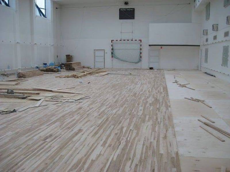 Na zdjęciu widzimy pomieszczenie sali sportowej podczas procesu układania drewnianego parkietu.