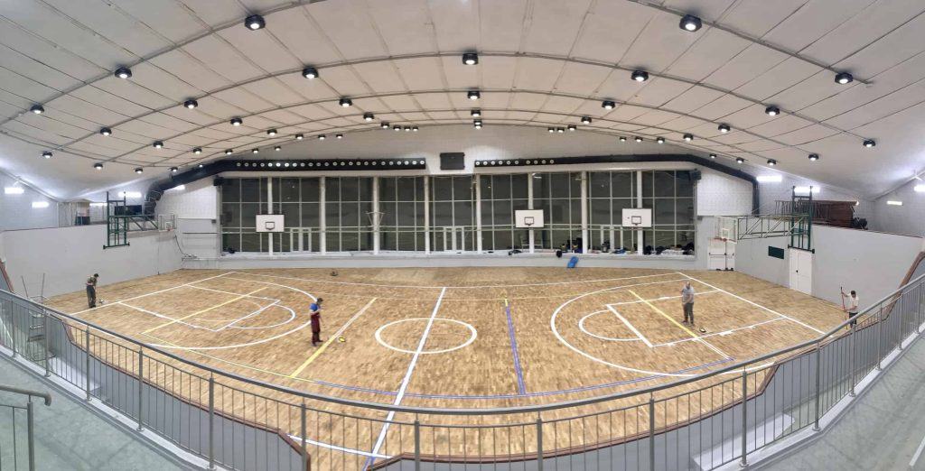 Zdjęcie wykonane z góry przedstawia halę sportową. Na jej drewnianej podłodze dwóch naszych ekspertów maluje linie boisk.
